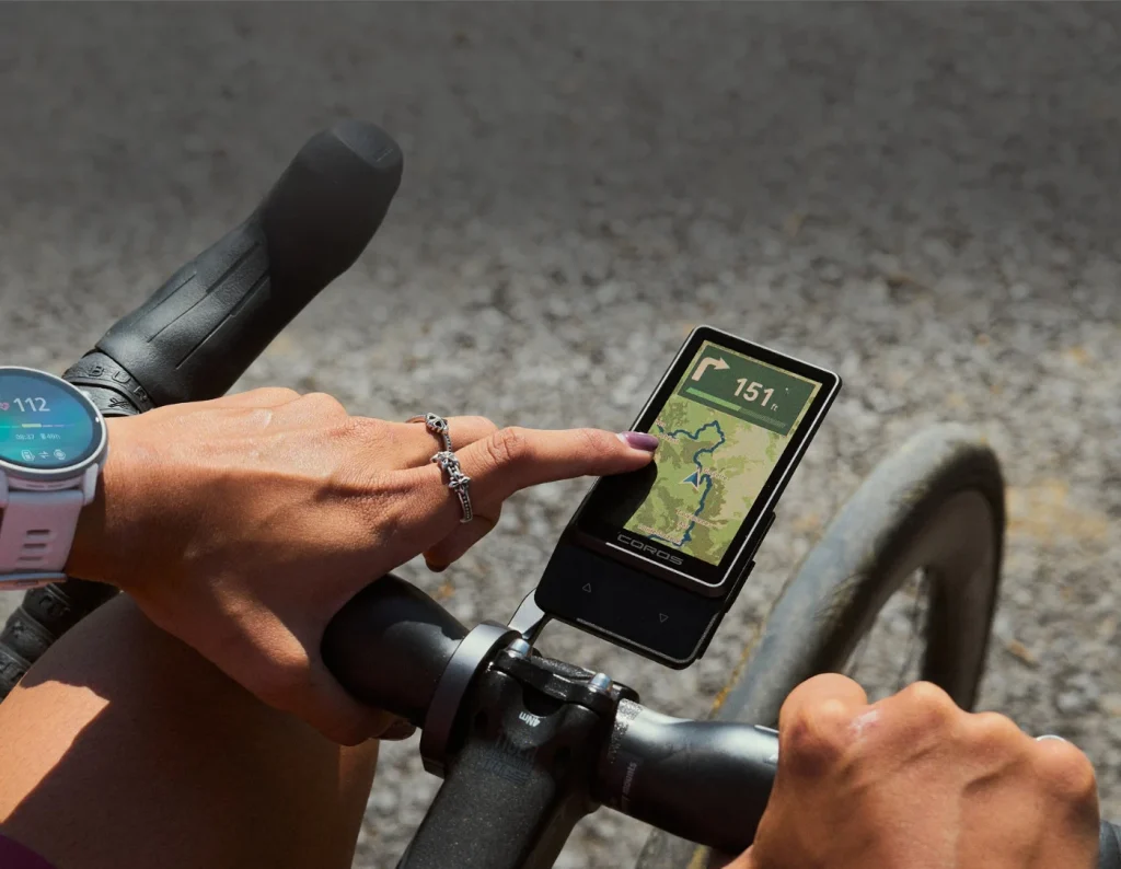 Ciclista manejando con el dedo la pantalla táctil del ciclocomputador de COROS montado en el manillar